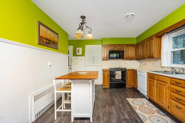 kitchen with radiator, sink, a breakfast bar area, hanging light fixtures, and black appliances