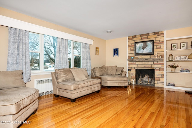 living room featuring hardwood / wood-style flooring, a stone fireplace, and radiator