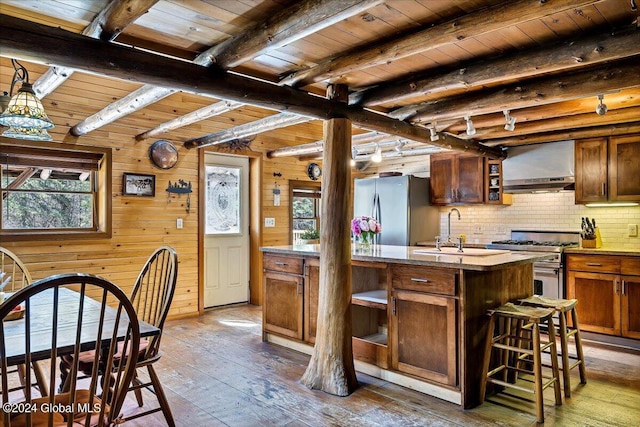 kitchen featuring sink, dark wood-type flooring, appliances with stainless steel finishes, a kitchen island with sink, and beamed ceiling