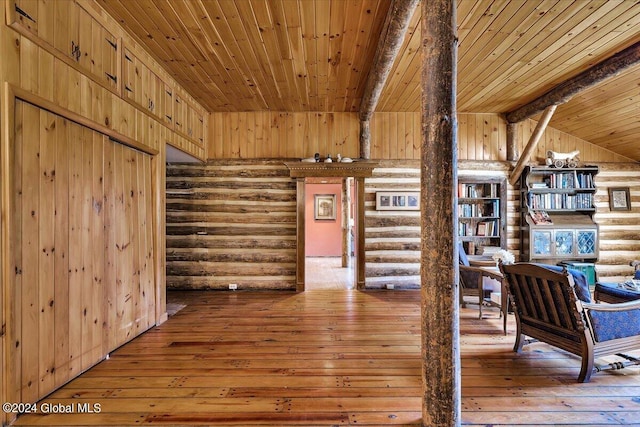 additional living space with wood-type flooring, lofted ceiling with beams, log walls, wooden ceiling, and wood walls