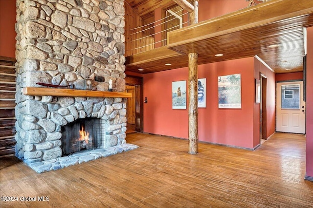 unfurnished living room featuring hardwood / wood-style flooring, a towering ceiling, a stone fireplace, and wooden ceiling