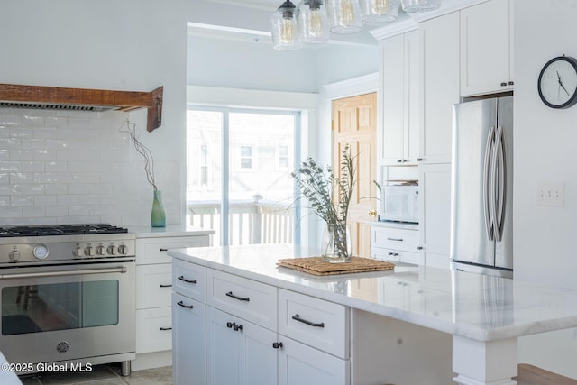 kitchen featuring light stone counters, stainless steel appliances, a kitchen island, white cabinetry, and decorative backsplash