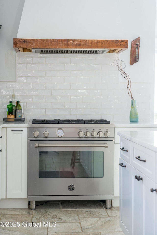 kitchen with white cabinets, custom range hood, stainless steel range, and backsplash