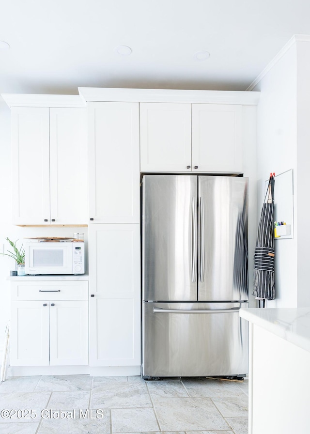 kitchen with white microwave, white cabinetry, ornamental molding, freestanding refrigerator, and light stone countertops