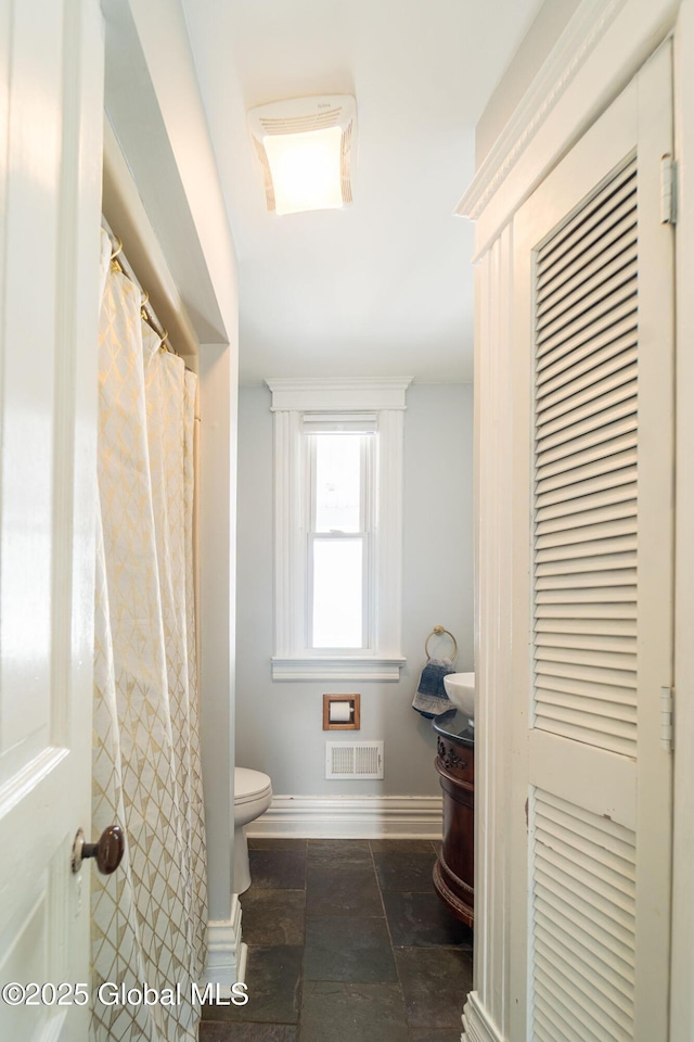 full bath featuring stone tile floors, visible vents, baseboards, toilet, and vanity