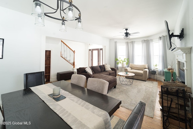 dining space with ceiling fan with notable chandelier, light wood finished floors, stairway, and a fireplace