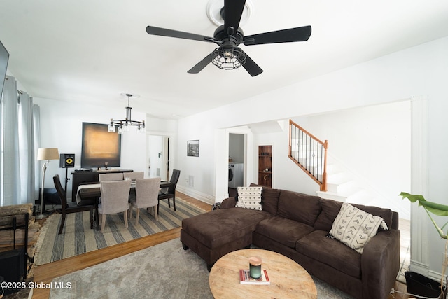 living room with washer / dryer, baseboards, stairway, wood finished floors, and ceiling fan with notable chandelier