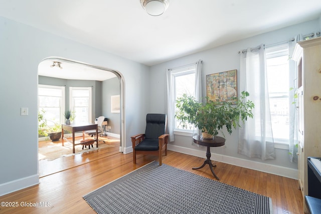 living area with arched walkways, light wood-style flooring, and baseboards