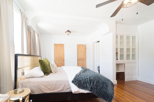 bedroom with a ceiling fan, built in study area, baseboards, and wood finished floors