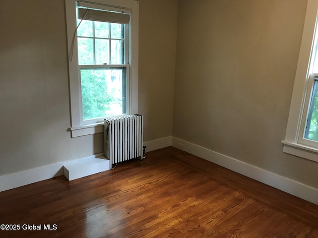 spare room with dark hardwood / wood-style flooring, a wealth of natural light, and radiator heating unit