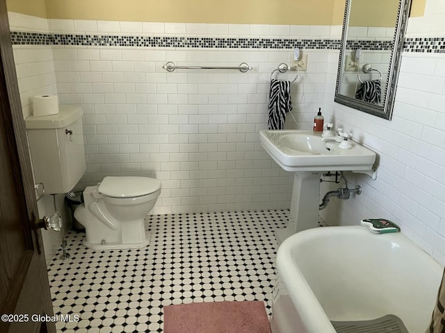 bathroom with tile patterned floors, toilet, sink, tile walls, and a washtub