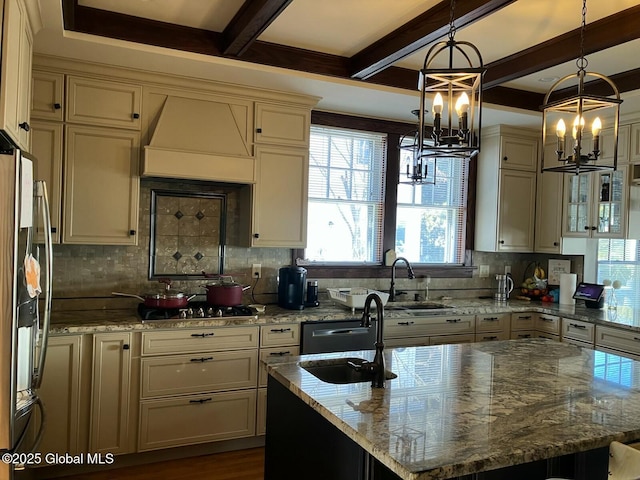 kitchen featuring sink, an island with sink, pendant lighting, light stone countertops, and cream cabinets