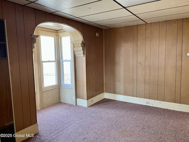 carpeted empty room featuring a paneled ceiling and wood walls