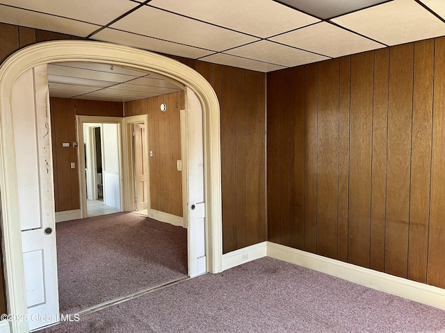 interior space featuring carpet, a drop ceiling, and wood walls