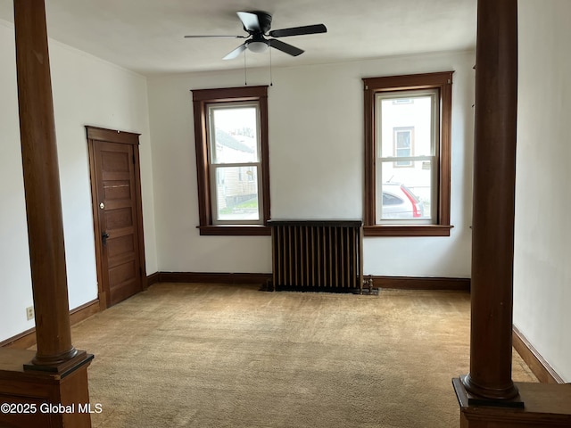 carpeted empty room with ornate columns, a healthy amount of sunlight, radiator heating unit, and ceiling fan