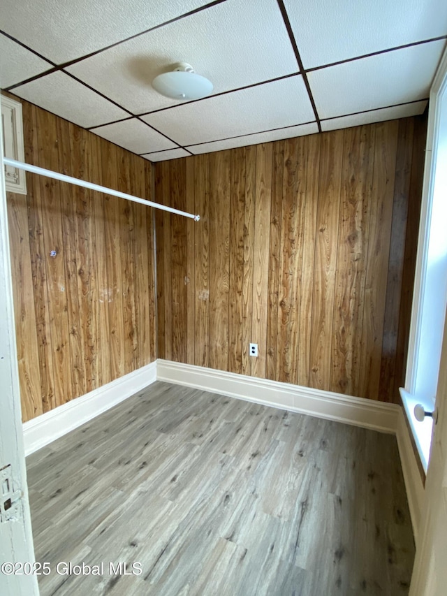 unfurnished room featuring hardwood / wood-style flooring, a drop ceiling, and wooden walls