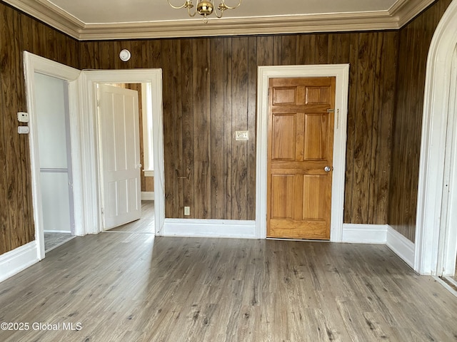 empty room with a notable chandelier, ornamental molding, and light wood-type flooring