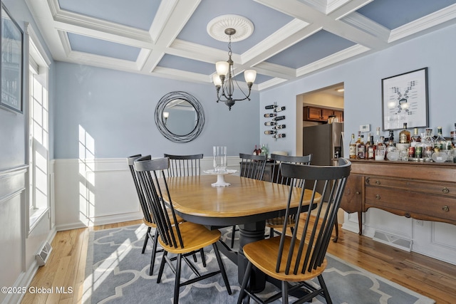 dining space featuring hardwood / wood-style flooring, coffered ceiling, an inviting chandelier, and beam ceiling