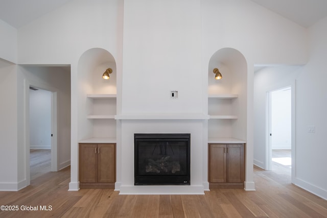 unfurnished living room featuring high vaulted ceiling, light hardwood / wood-style floors, and built in features