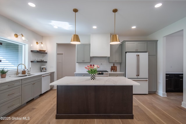 kitchen featuring sink, white appliances, light stone counters, custom range hood, and a kitchen island