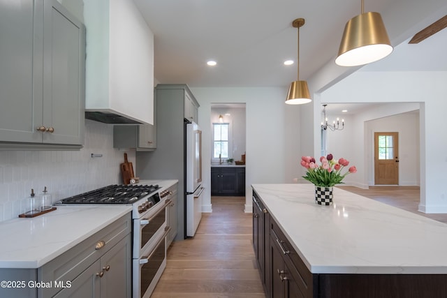 kitchen featuring pendant lighting, gray cabinetry, decorative backsplash, light stone countertops, and white appliances