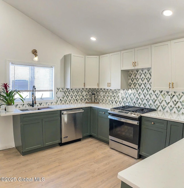 kitchen with appliances with stainless steel finishes, lofted ceiling, sink, white cabinets, and decorative backsplash