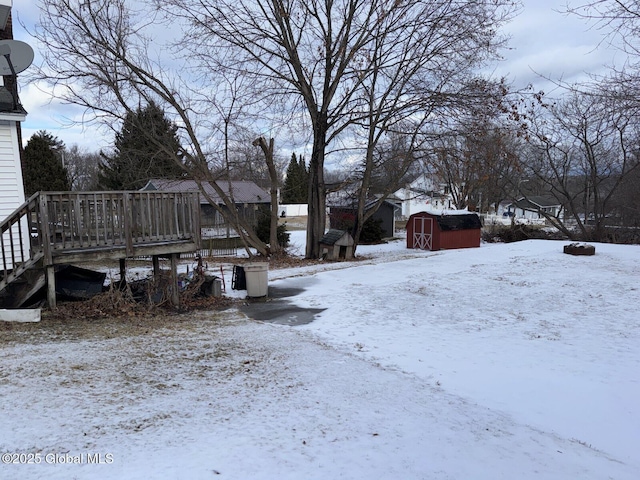 yard covered in snow featuring a wooden deck and a storage shed