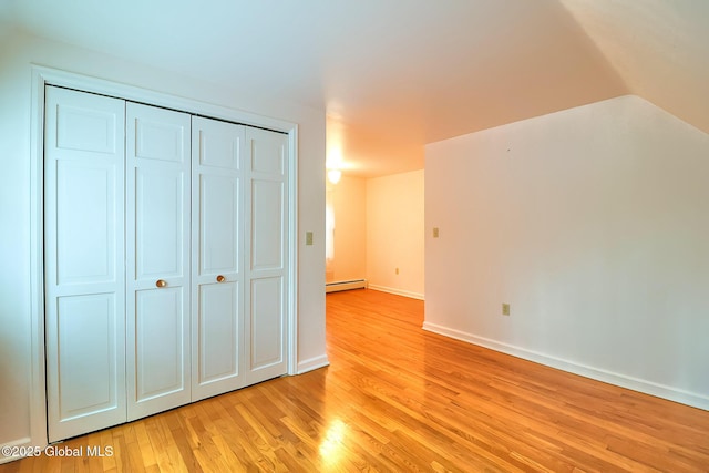 unfurnished bedroom featuring lofted ceiling, light hardwood / wood-style floors, a closet, and baseboard heating