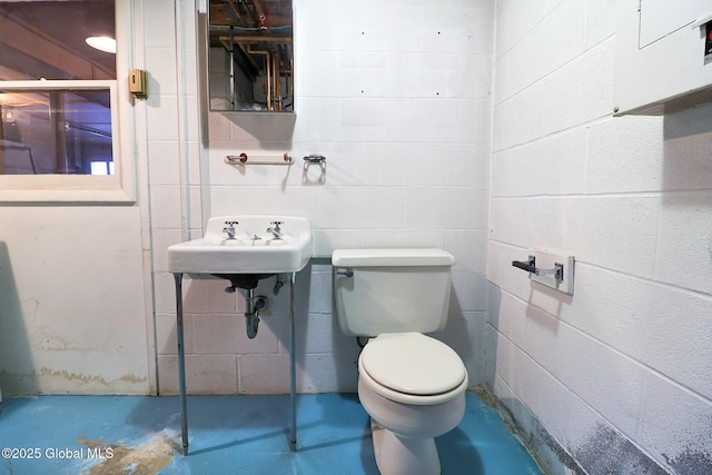 bathroom with toilet, concrete flooring, and sink