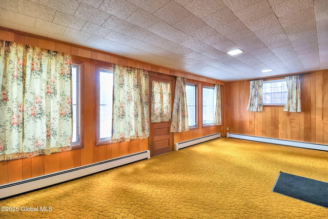 carpeted empty room featuring baseboard heating and wooden walls