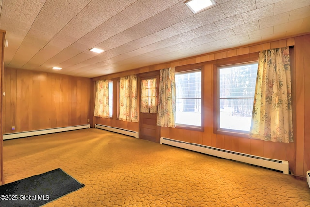 carpeted spare room with a baseboard heating unit and wood walls