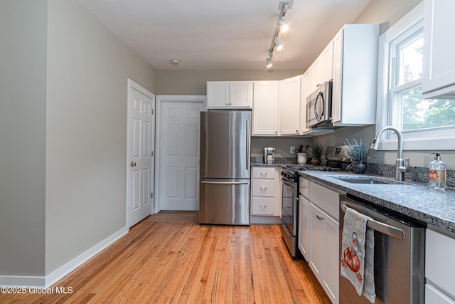 kitchen with appliances with stainless steel finishes, sink, white cabinets, and light hardwood / wood-style flooring