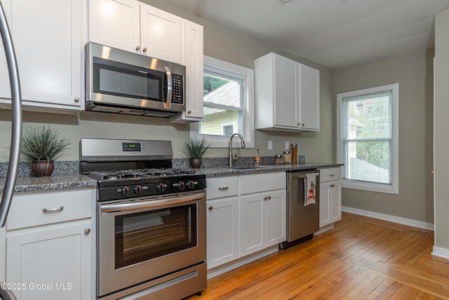 kitchen with white cabinetry, appliances with stainless steel finishes, sink, and dark stone countertops