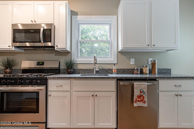 kitchen with white cabinetry, stainless steel appliances, sink, and dark stone countertops