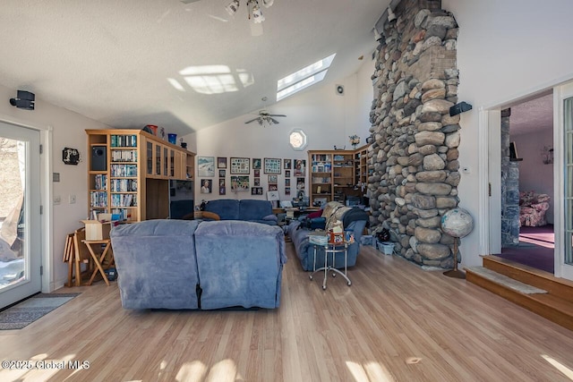 living room with high vaulted ceiling, light wood-type flooring, ceiling fan, and a skylight