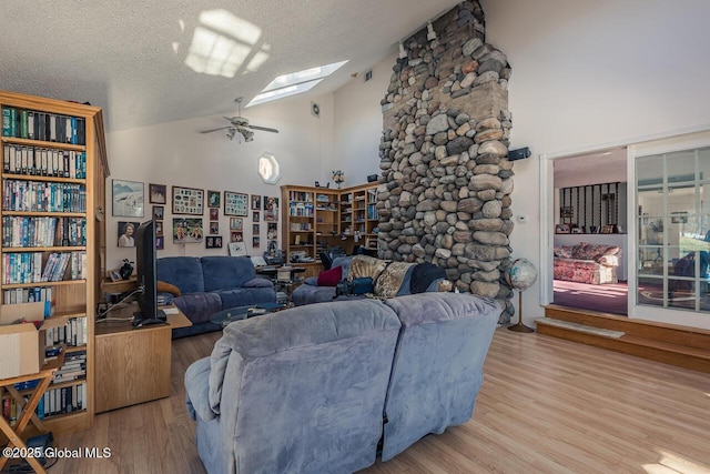 living room with high vaulted ceiling, a skylight, ceiling fan, light hardwood / wood-style floors, and a textured ceiling