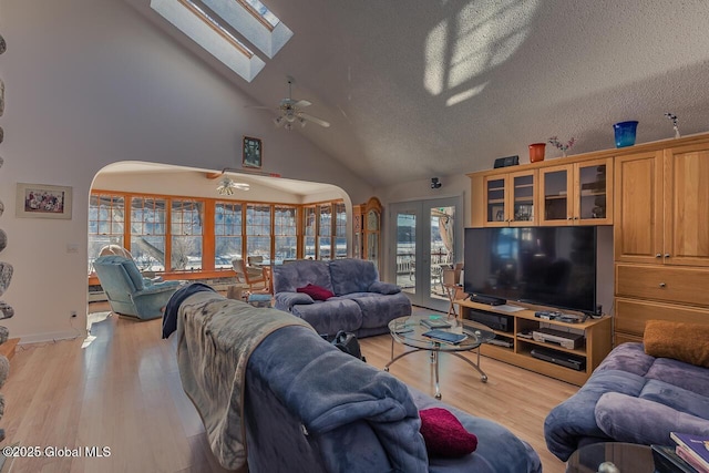 living room featuring ceiling fan, a skylight, light hardwood / wood-style floors, a textured ceiling, and french doors