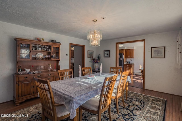 dining area featuring dark hardwood / wood-style floors, a textured ceiling, and an inviting chandelier