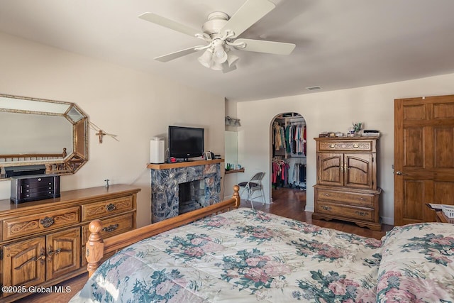 bedroom with dark wood-type flooring, a spacious closet, a closet, ceiling fan, and a fireplace