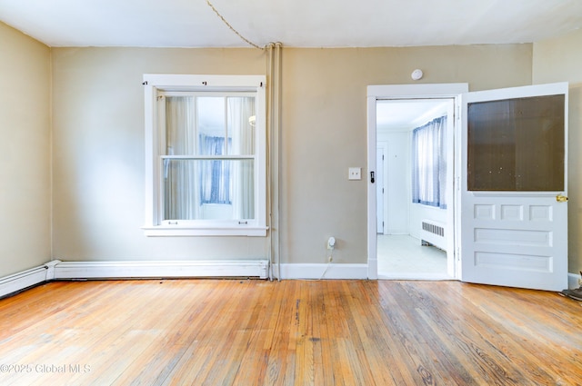 empty room with a baseboard radiator, radiator heating unit, and light hardwood / wood-style flooring