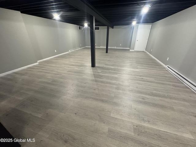 basement featuring a baseboard heating unit and hardwood / wood-style flooring