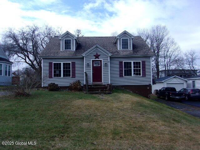 cape cod-style house with a garage, an outdoor structure, and a front lawn