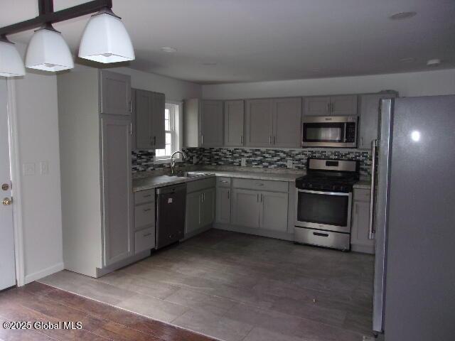 kitchen featuring gray cabinets, pendant lighting, sink, decorative backsplash, and stainless steel appliances
