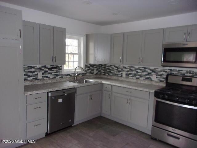 kitchen featuring stainless steel appliances, sink, gray cabinetry, and decorative backsplash