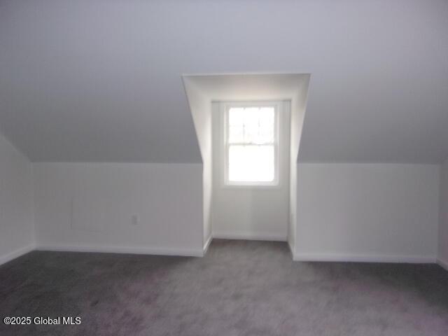 additional living space featuring lofted ceiling and dark colored carpet