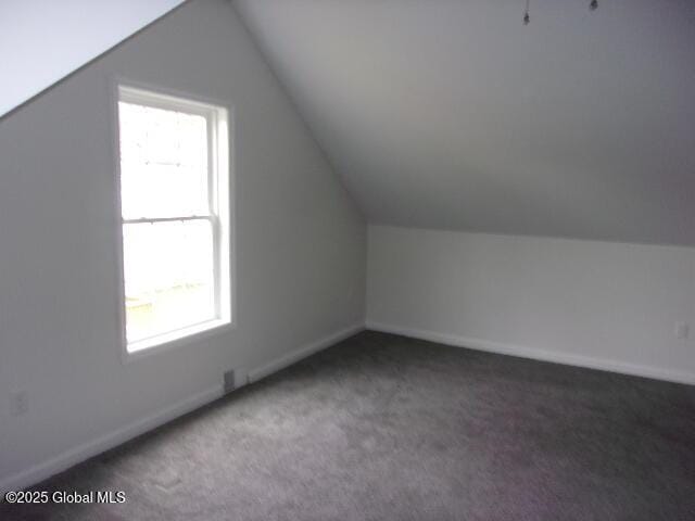 additional living space with vaulted ceiling, a healthy amount of sunlight, and dark carpet