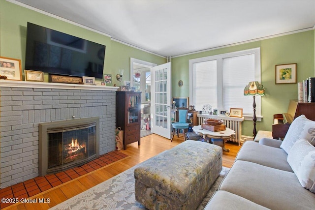 living room featuring ornamental molding, radiator, light hardwood / wood-style floors, and a brick fireplace