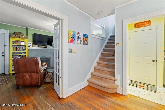 stairway with a brick fireplace, crown molding, and wood-type flooring