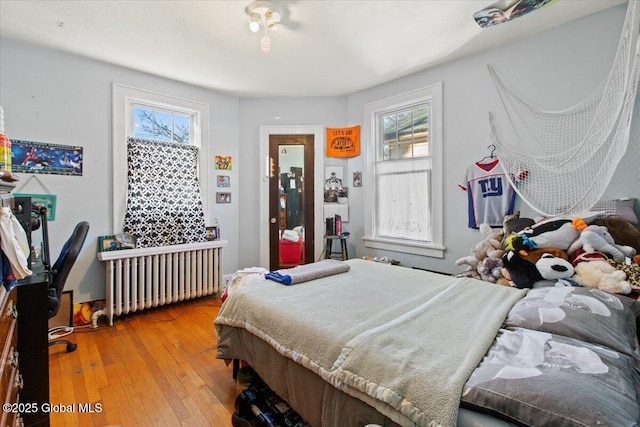 bedroom with multiple windows, radiator heating unit, and wood-type flooring