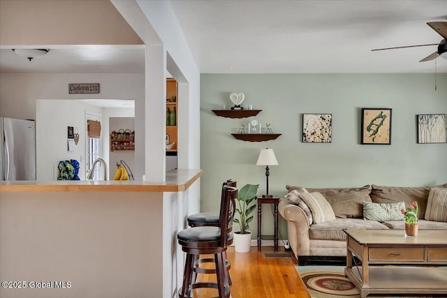 living room with ceiling fan, sink, and light wood-type flooring